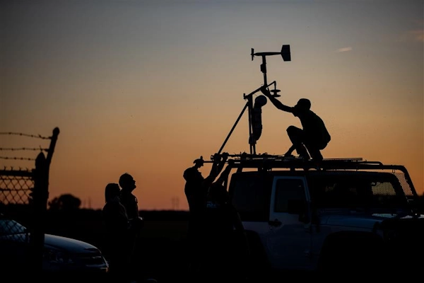 Dusk falls on people adjusting scientific instruments on a vehicle