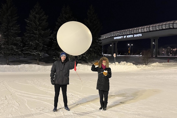 Two people prepare for a balloon launch at night during the winter