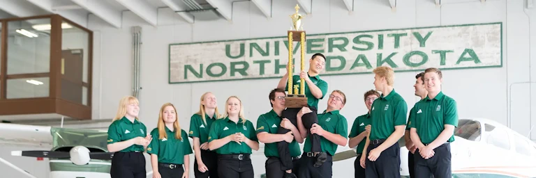 The UND Flying Team celebrates with a trophy in the hangar