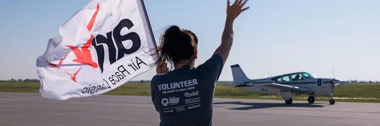An Air Race Classic event volunteer waves at a departing airplane