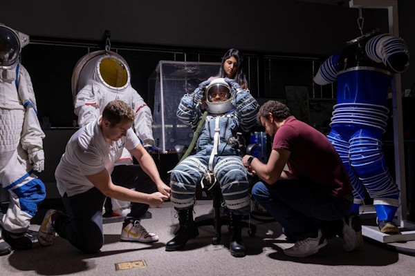 People assist while a person tries on a space suit
